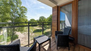 A balcony with wicker furniture, a glass door, and a view of trees and a grassy area. - Apartamenty Sun & Snow Enklawa III (Mielno)
