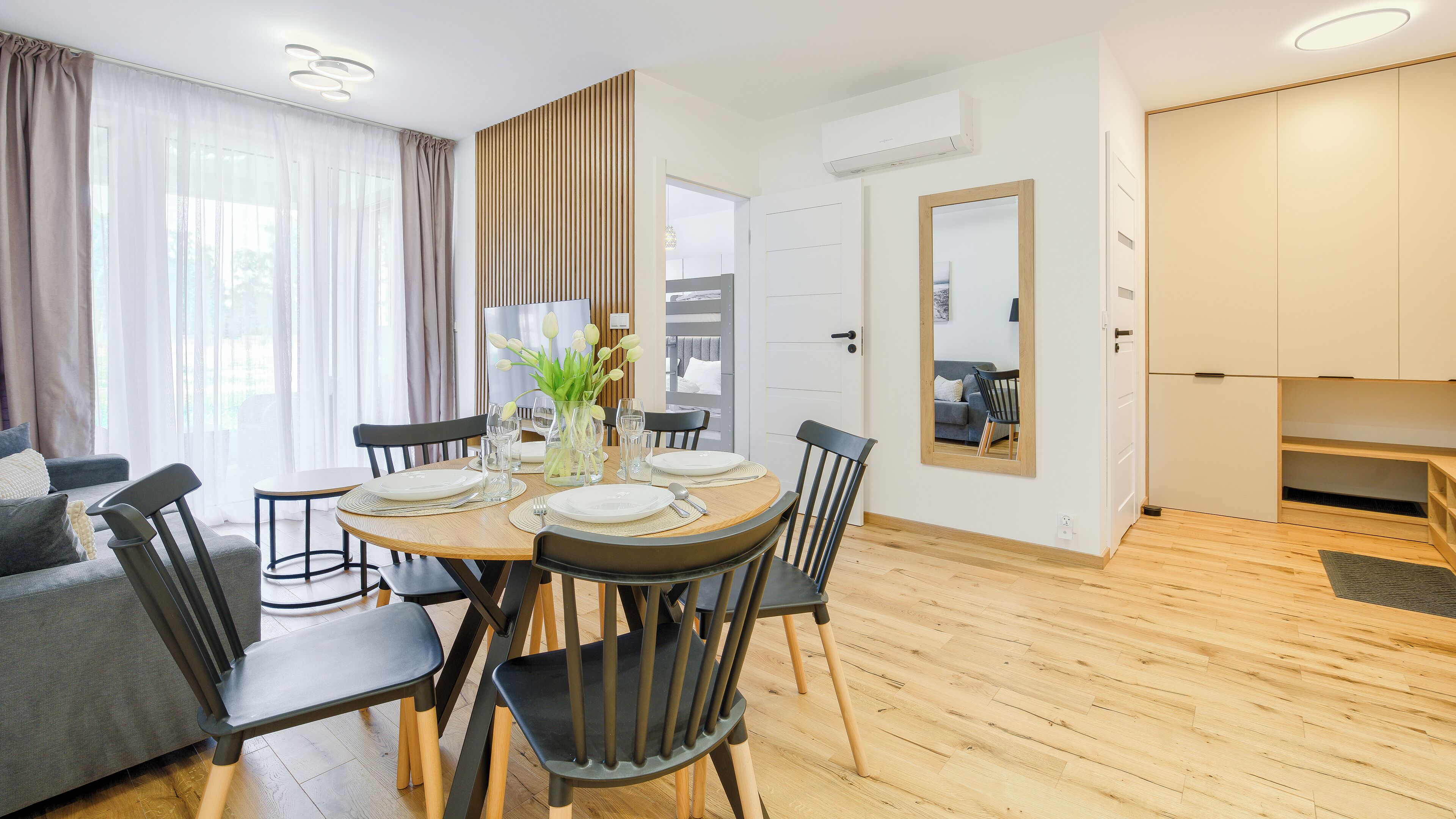 Una sala de estar moderna con comedor, suelo de madera y un espejo grande.