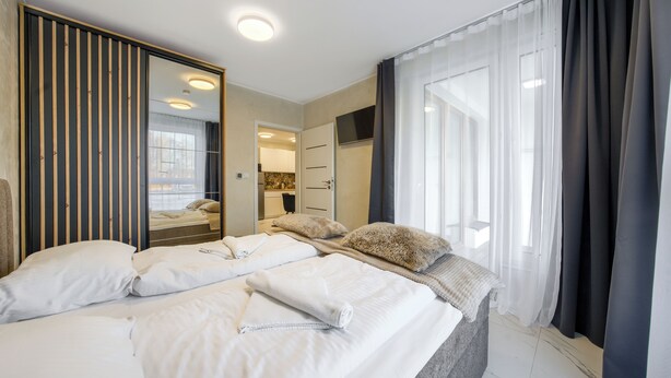 A hotel room with a large bed, a mirror, a wardrobe, and a bathroom visible through an open door. - Apartamenty Sun & Snow Enklawa III (Mielno)