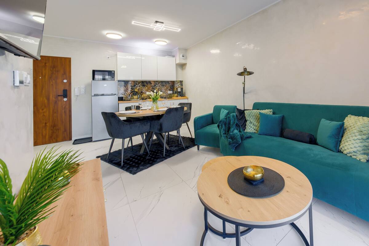 Una sala moderna con un sofá azul turquesa, una mesa de centro redonda y un comedor con mesa y sillas de madera.