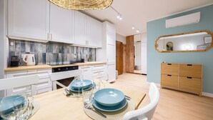 A modern kitchen with white cabinets, a wooden countertop, and a dining area set with blue plates and glasses. - Apartamenty Sun & Snow Enklawa III (Mielno)