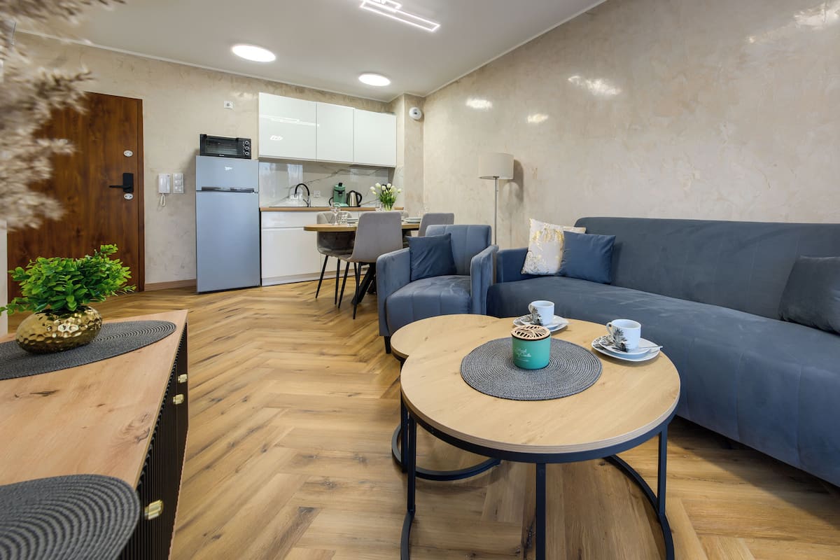 Una sala de estar moderna con un sofá, dos mesas de centro y un comedor con una cocina al fondo.