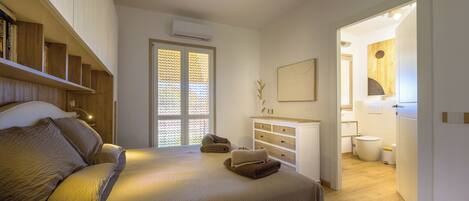 A bedroom with a bed, a dresser, a window with blinds, and a bathroom visible through an open door.