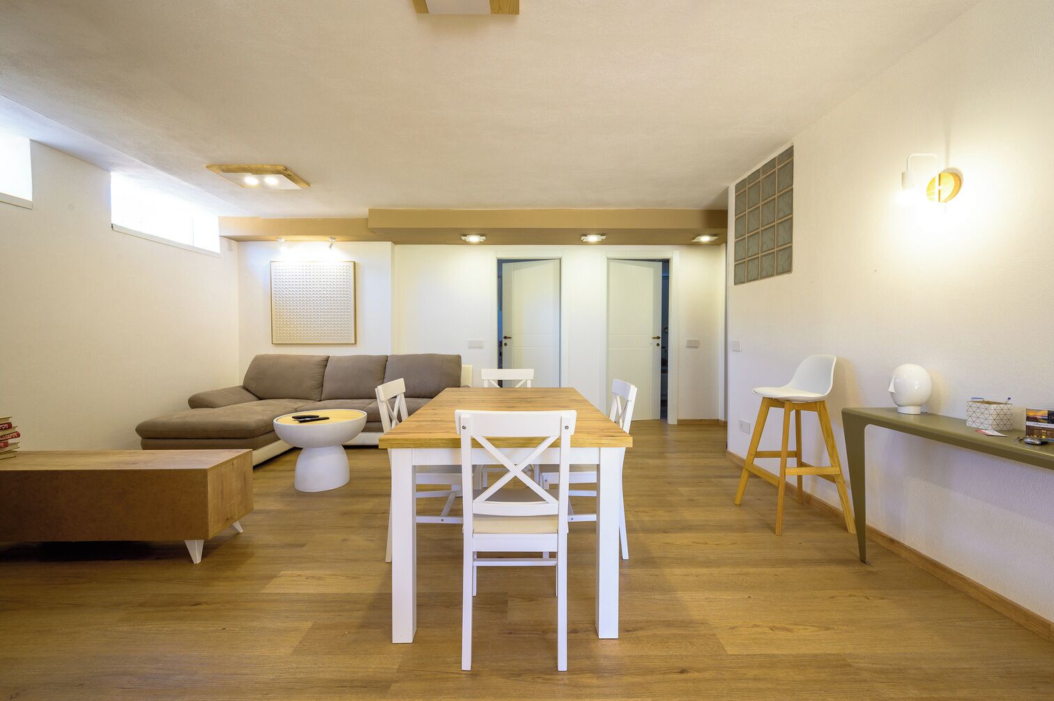 A modern living room with a wooden dining table, white chairs, a sofa, and a coffee table.