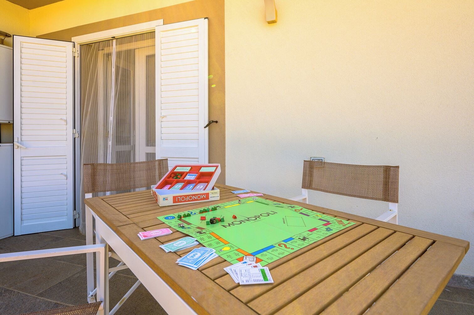 A wooden table with a Monopoly board game, chairs, and a closed door with blinds.
