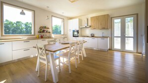 A modern kitchen with wooden flooring, white cabinetry, and a dining area with a wooden table and chairs. - Sunset Villa - Entire Structure (Alghero)
