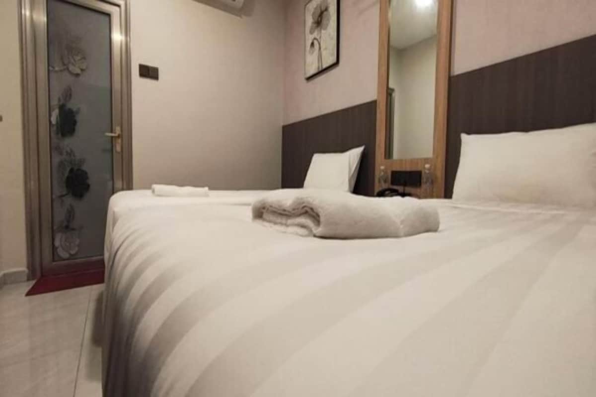 A neatly made bed with a white comforter and pillows, a wooden headboard, and a glass shower door with floral patterns.