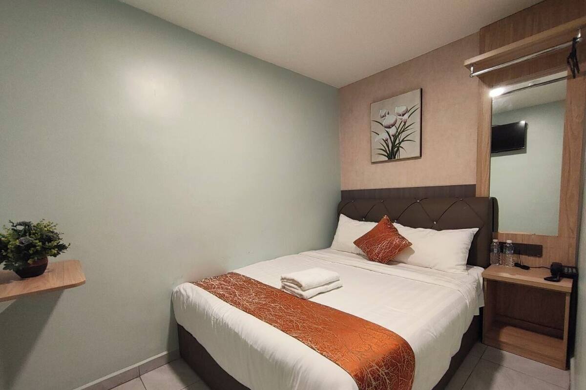 Un llit ben fet amb un edredó blanc i taronja, una petita taula de nit amb una ampolla i un televisor fixat a la paret.