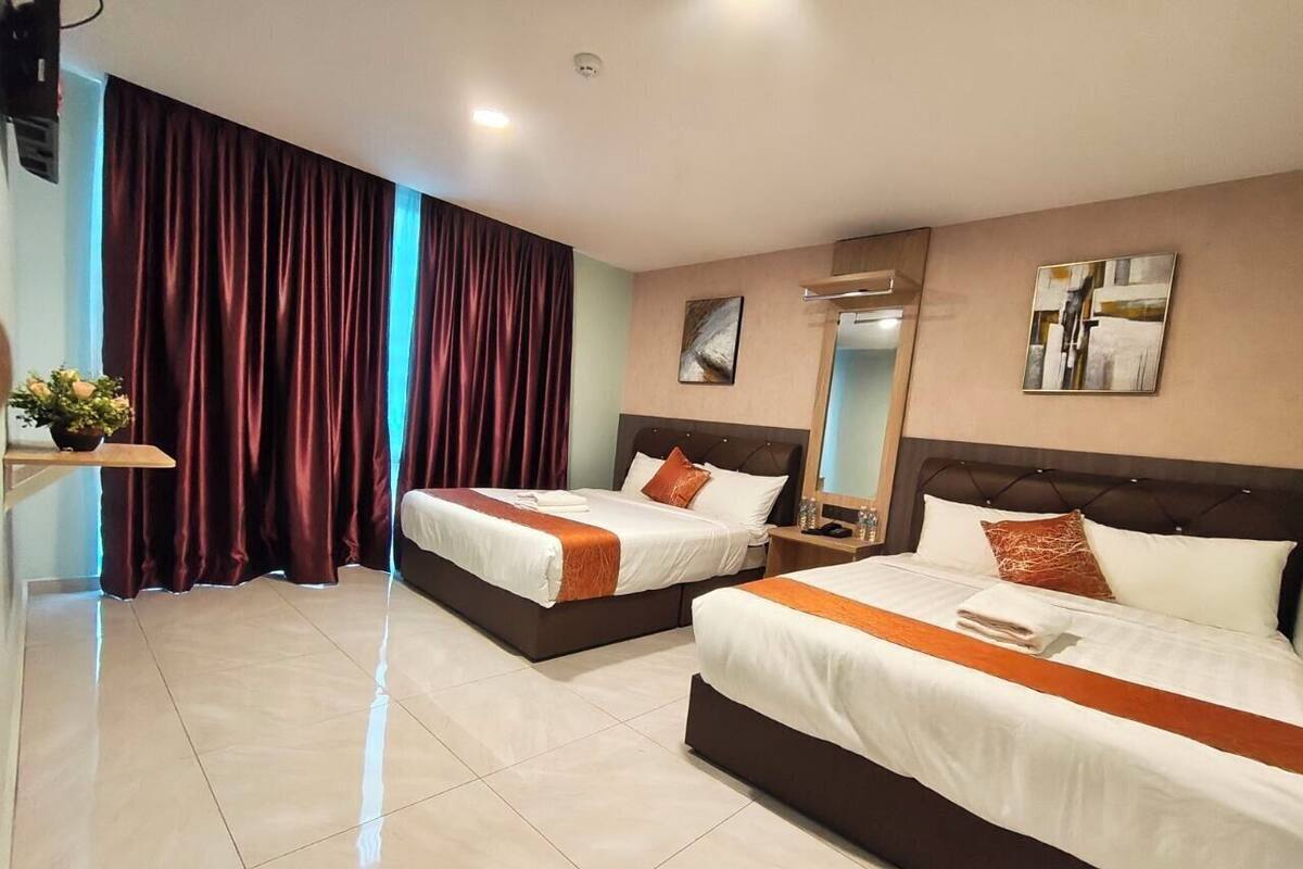 Habitació d'hotel amb dos llits, un gran finestral amb cortines, una taula de nit amb làmpada i una obra d'art penjada a la paret.