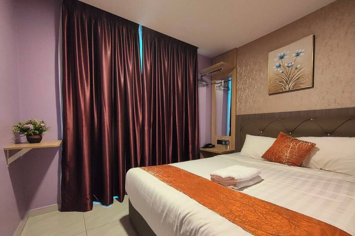 Habitació d'hotel amb un llit gran, una tauleta de nit, un mirall, un quadre penjat a la paret i una cortina.