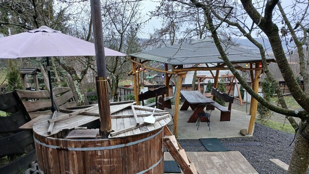 Un espacio exterior rústico con un barril de madera, mesas de picnic y una construcción de madera con techo.