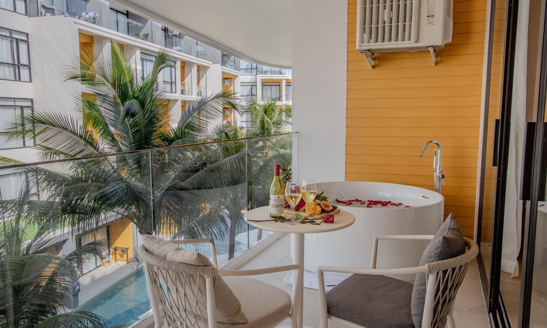 A balcony with a white bathtub, a table with drinks, and chairs.