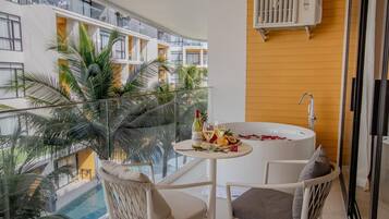 A balcony with a white bathtub, a table with drinks, and chairs.