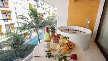 A balcony with a pool, a bathtub with rose petals, a bottle of wine, a pineapple, a glass of wine, a glass of champagne, and a rose.