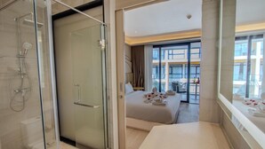 A modern hotel room with a glass shower enclosure, a bed with towels, and a view of the city through large windows. - 2314 1BR Wyndham Naithon (Sa Khu)