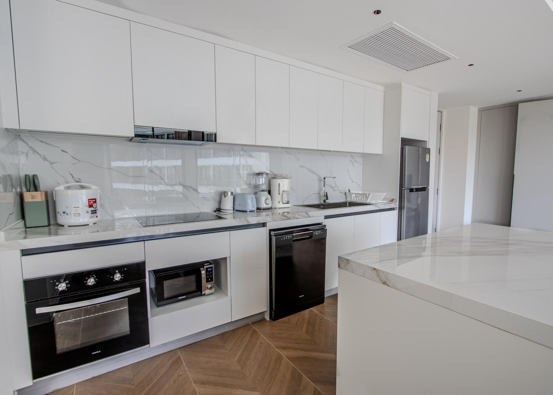 Una cocina moderna con armarios blancos, encimera de mármol, horno empotrado, lavavajillas y refrigerador.
