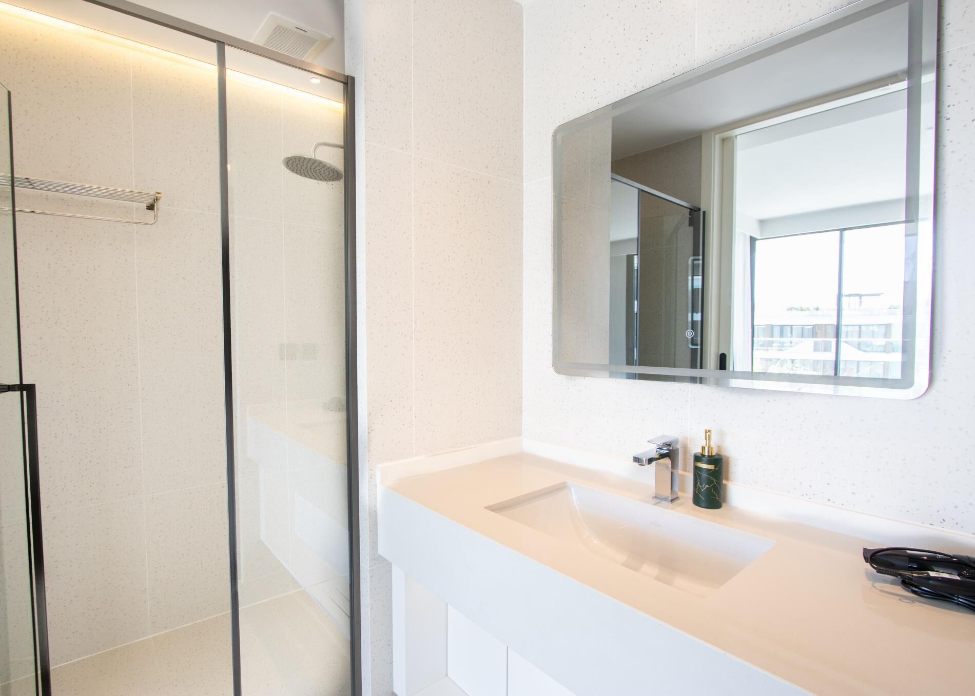 Un baño moderno con ducha envuelta en vidrio, un lavabo blanco y un espejo grande.