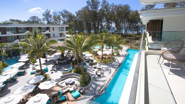 Zona de piscina en un resort con sillas de descanso, sombrillas y palmeras.