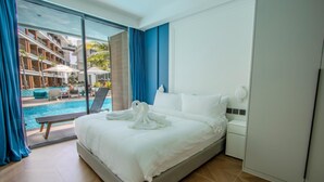 A hotel room with a bed, a nightstand, a wardrobe, and a view of a swimming pool and outdoor seating area. - 189/222 3BR Beachfront Luxe Pool Access (Choeng Thale)