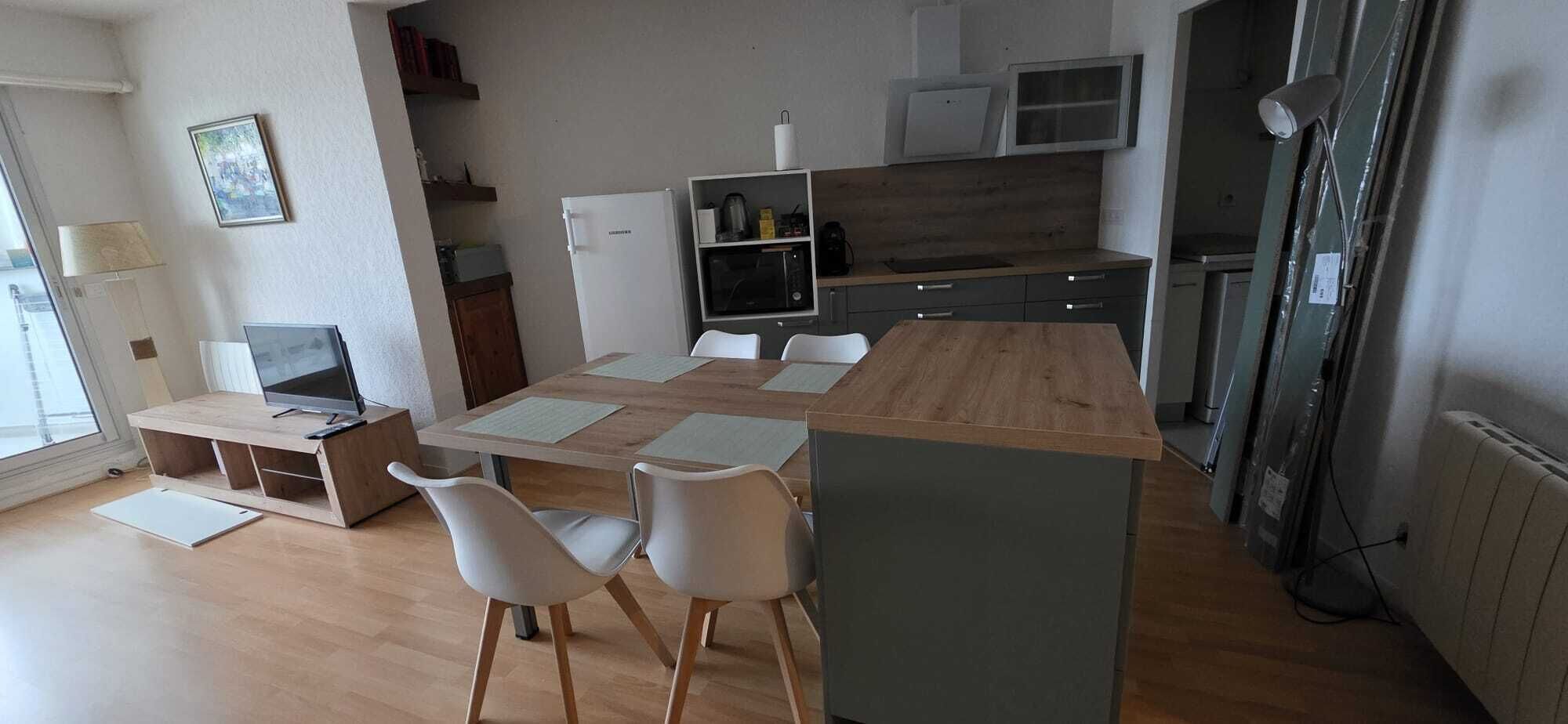 Moderni keittiö, jossa on ruokailutila. Tilaan kuuluu puinen pöytä, valkoiset tuolit, mikroaaltouuni ja jääkaappi.