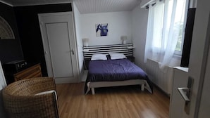 Een slaapkamer met een bed, een stoel, een deur, een raam en een aan de muur bevestigd schilderij.