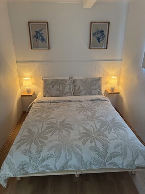 A bedroom with a bed, two bedside lamps, a headboard, and two framed artworks on the wall.