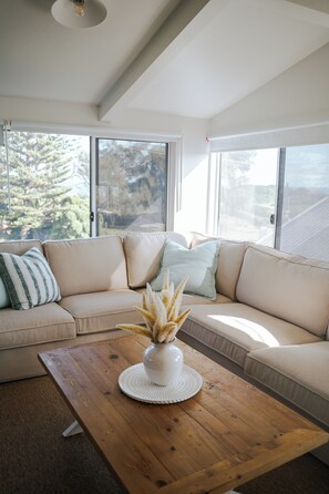 A modern living room with a sectional sofa, a wooden coffee table, and large windows offering a view of trees.