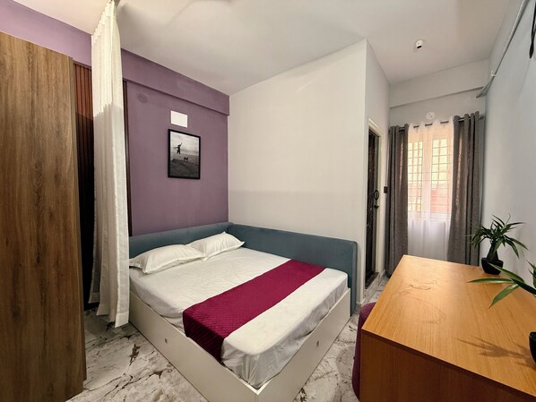 A bedroom with a bed, a wooden desk, a potted plant, and a window with curtains. - C SUITES Colive 1263 Bren (Bengaluru)