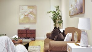 Ein Wohnzimmer mit einer Couch, einem Beistelltisch mit Lampe, einer Zimmerpflanze und abstrakter Kunst an den Wänden.