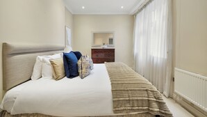 Ein Schlafzimmer mit einem Bett, einem Schminktisch, einem Spiegel und einem Fenster mit Vorhängen.