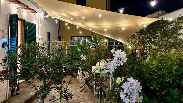 Een binnenplaats met een pergola, versierd met lichtslingers, omringd door potplanten en witte bloemen.