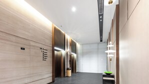 A modern elevator area with a marble floor, wooden paneling, and a green bowl on a counter. - Atour Hotel (Wuxi)