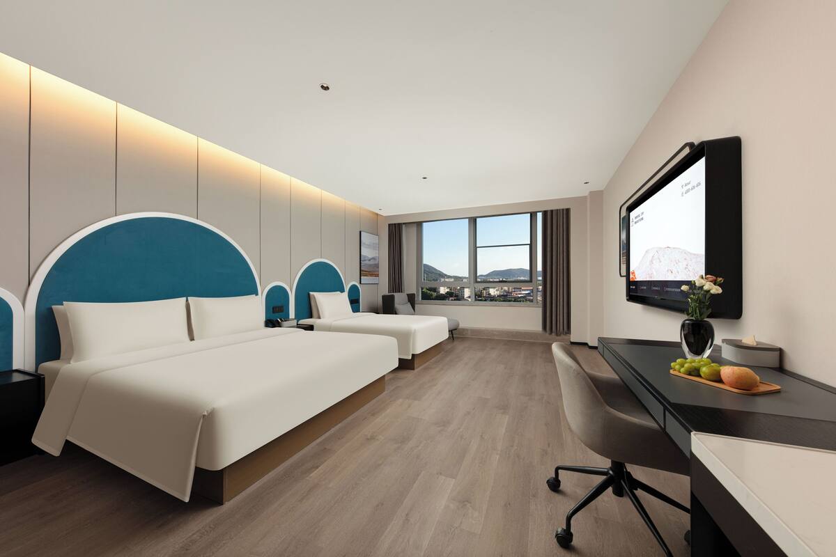 A modern hotel room with a large bed, a desk, a TV, and a view of the city.
