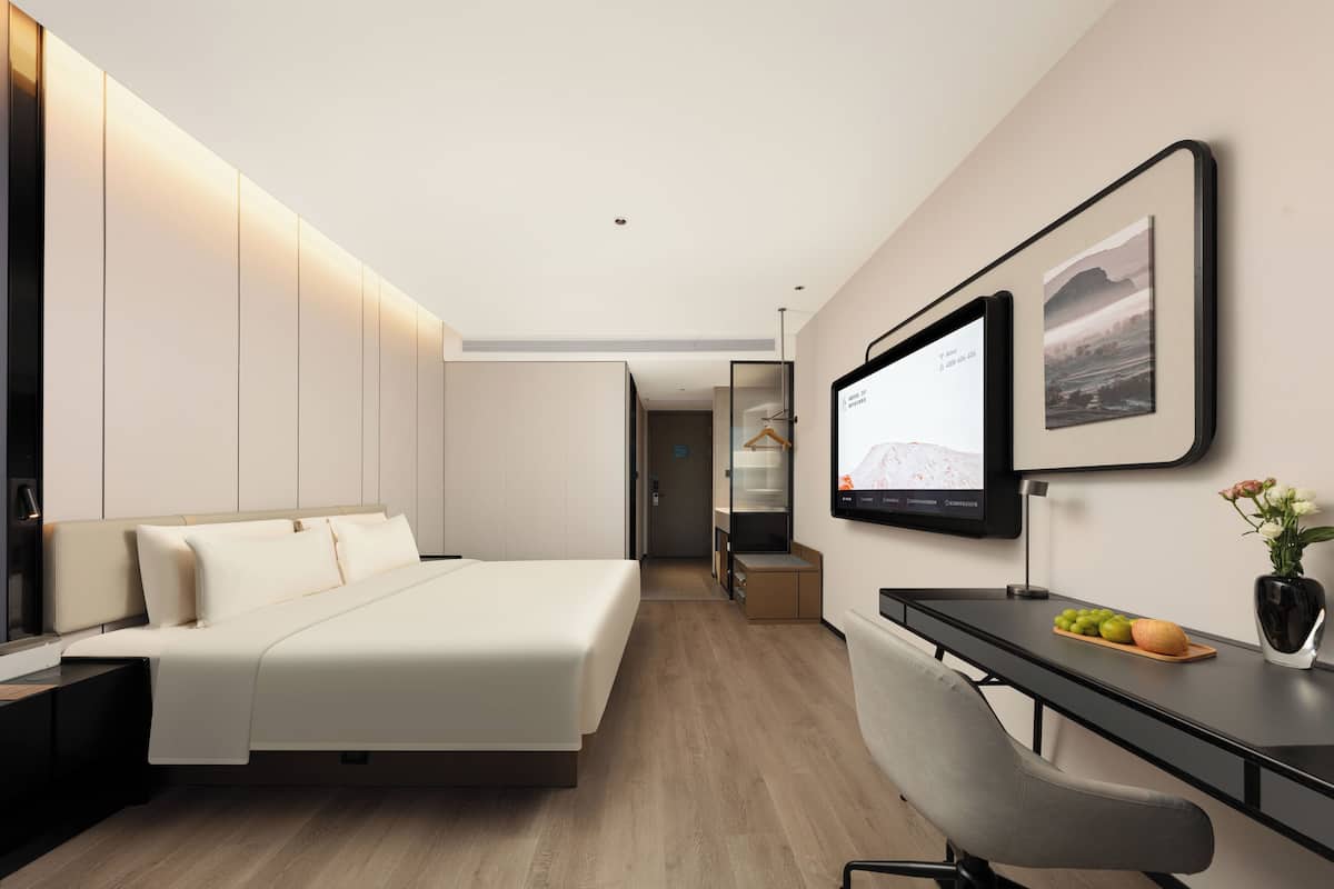 A modern hotel room with a bed, desk, and a television on the wall.