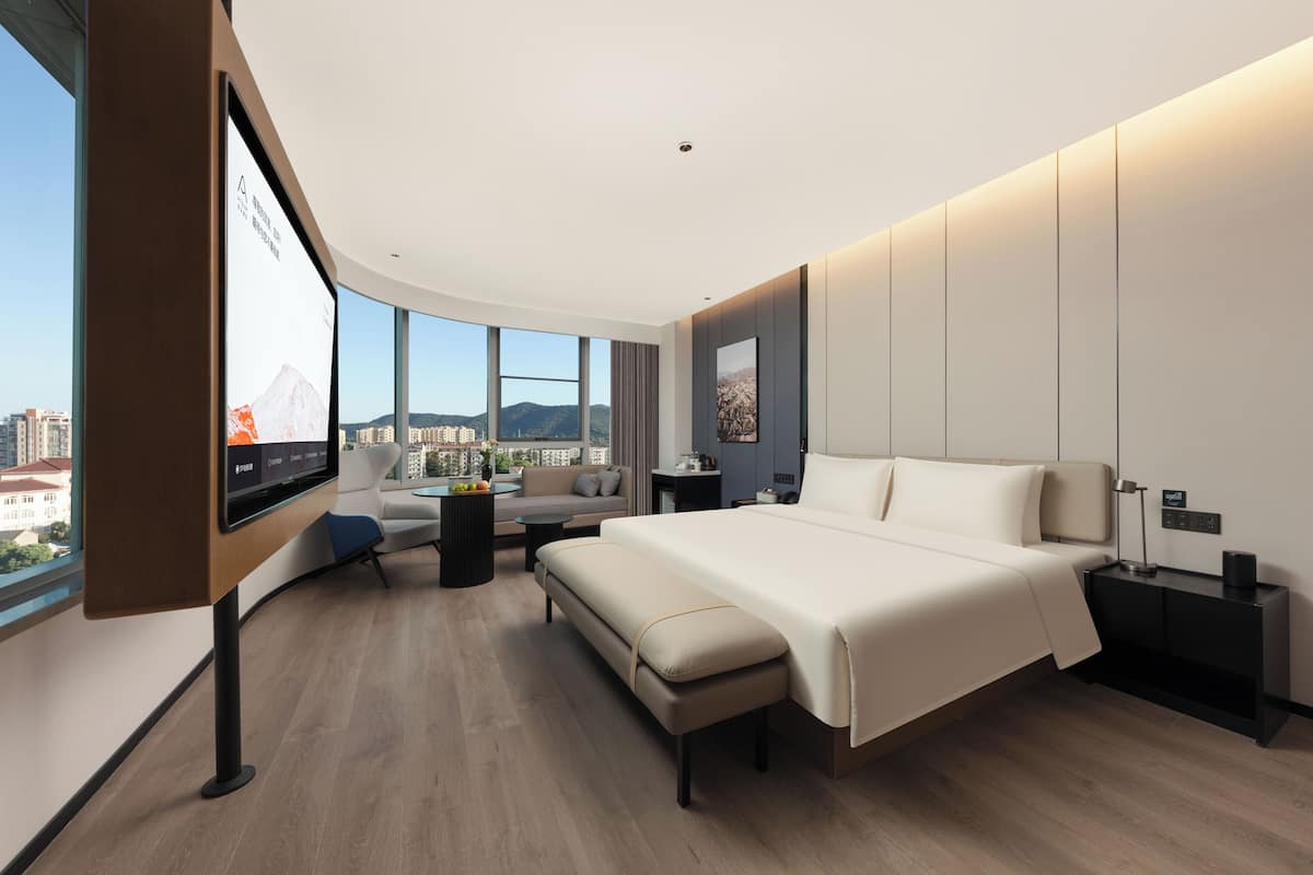 A modern hotel room with a large bed, a sofa, a small table, and a TV mounted on the wall.