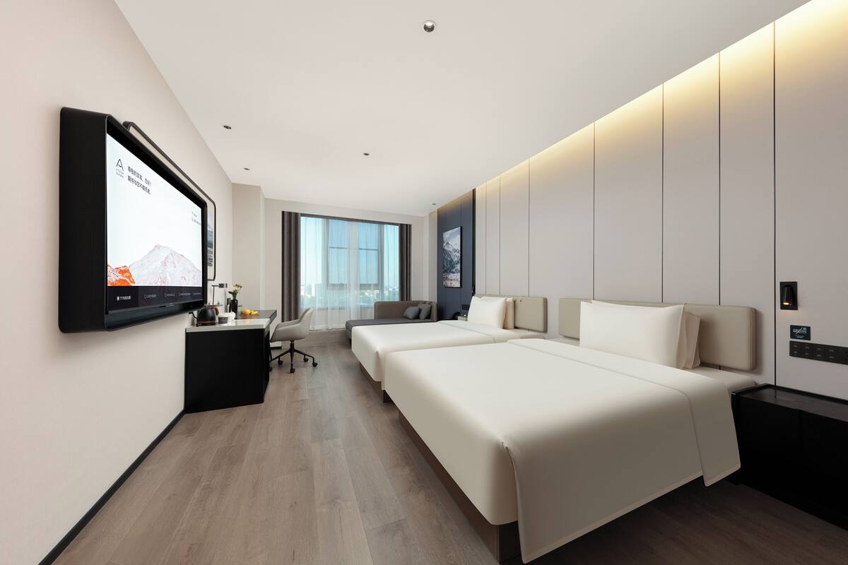 A modern hotel room with a large bed, a desk, a chair, and a flat-screen TV mounted on the wall.