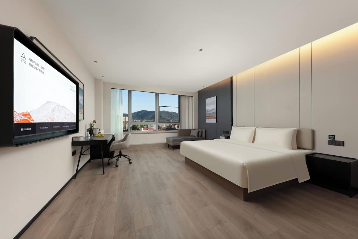 A modern hotel room with a large bed, a desk, and a television mounted on the wall.