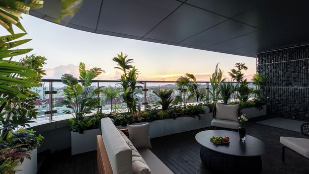 A rooftop terrace with a view of the city skyline at sunset, featuring a sofa, a round table, and potted plants. - Atour Hotel (Wuxi)