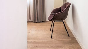 A modern room with a wooden floor, a large mirror, a chair, and a tall, narrow window with curtains. - Munich Finest Apartments Studio 4 by Interhome (Munich)