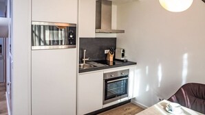 A compact kitchen with a built-in oven, a microwave, and a sink. There is a knife block on the countertop and a cup on the table. - Munich Finest Apartments Studio 4 by Interhome (Munich)