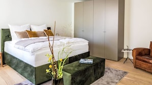 A modern bedroom with a large bed, a green accent wall, a minimalist wardrobe, and a leather armchair. - Munich Finest Apartments Studio 4 by Interhome (Munich)