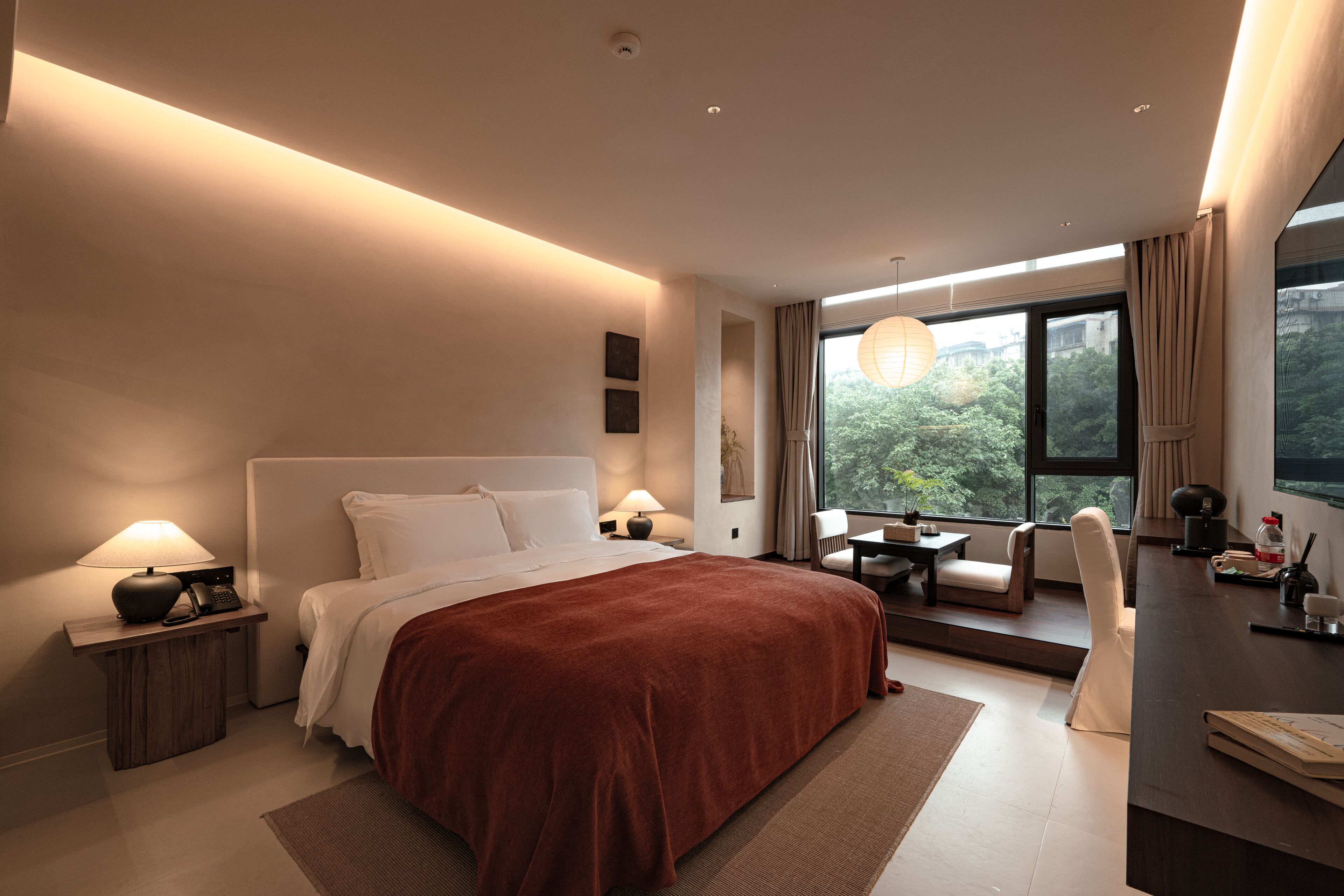 Una habitación de hotel moderna con una cama grande, lámparas de noche, un escritorio y vistas a zonas verdes por la ventana.