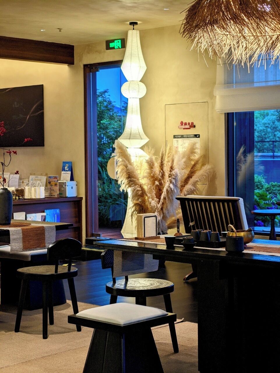 A reception area with a desk, chairs, a large decorative lamp, and a window with a view of greenery.