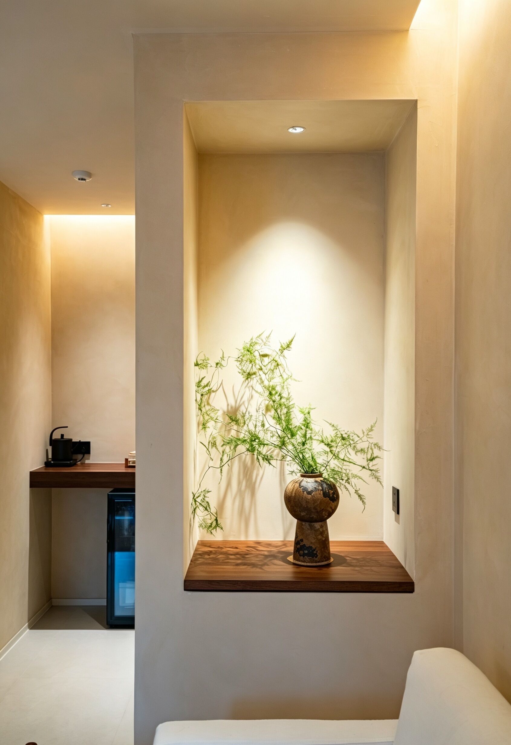Habitación minimalista con una repisa de madera que sostiene una planta en maceta, una pequeña mesa y una máquina de café.