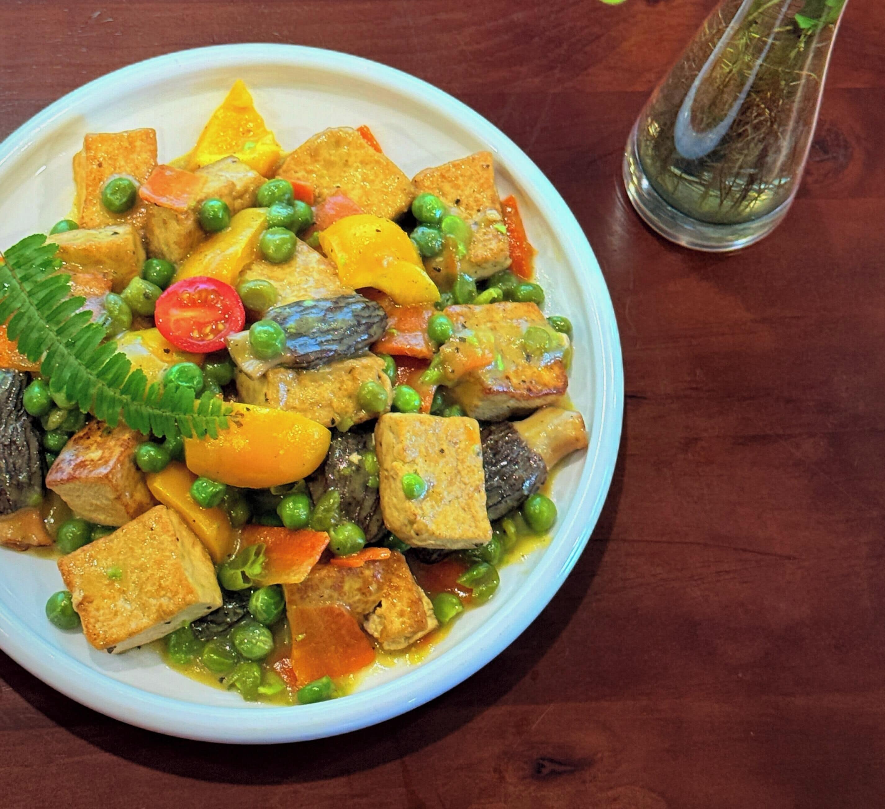 A plate of food with tofu, peas, carrots, and mushrooms.