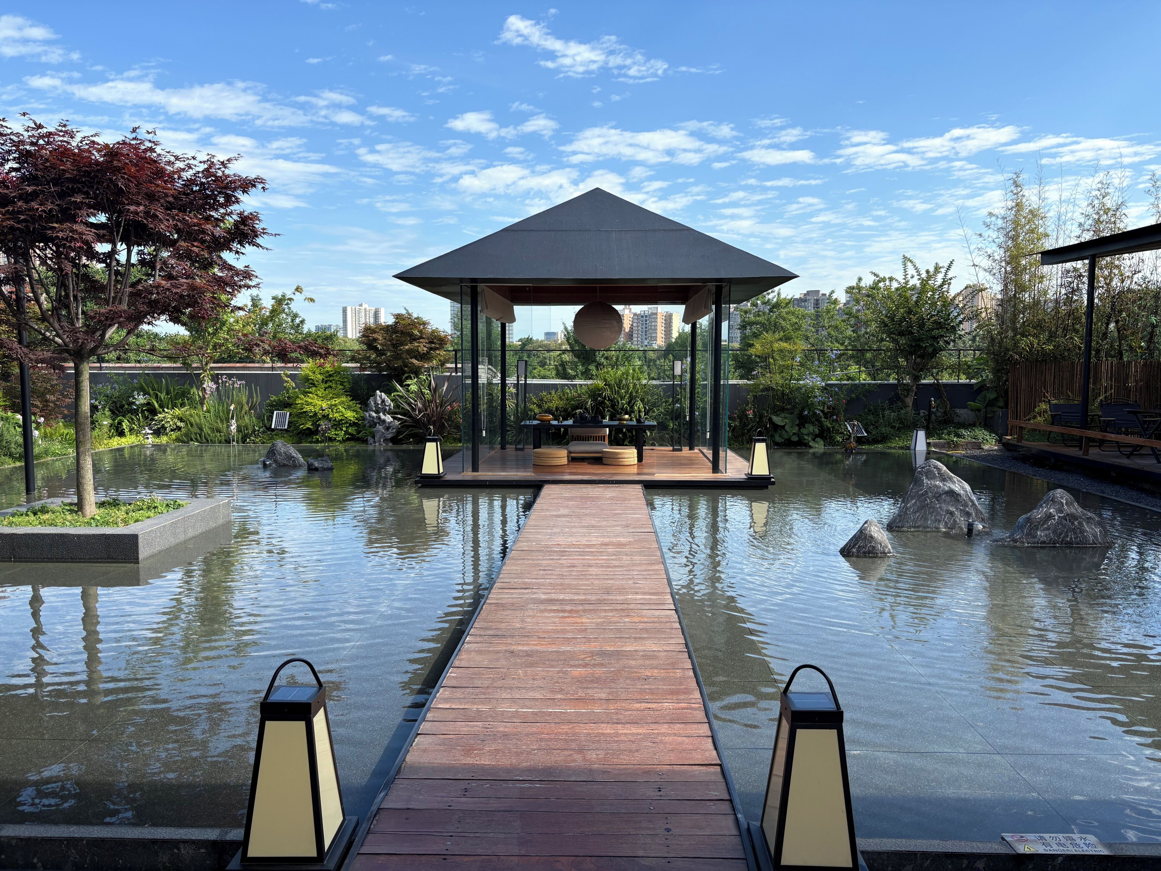 A modern outdoor pool area with a wooden deck, a gazebo, and surrounding greenery.