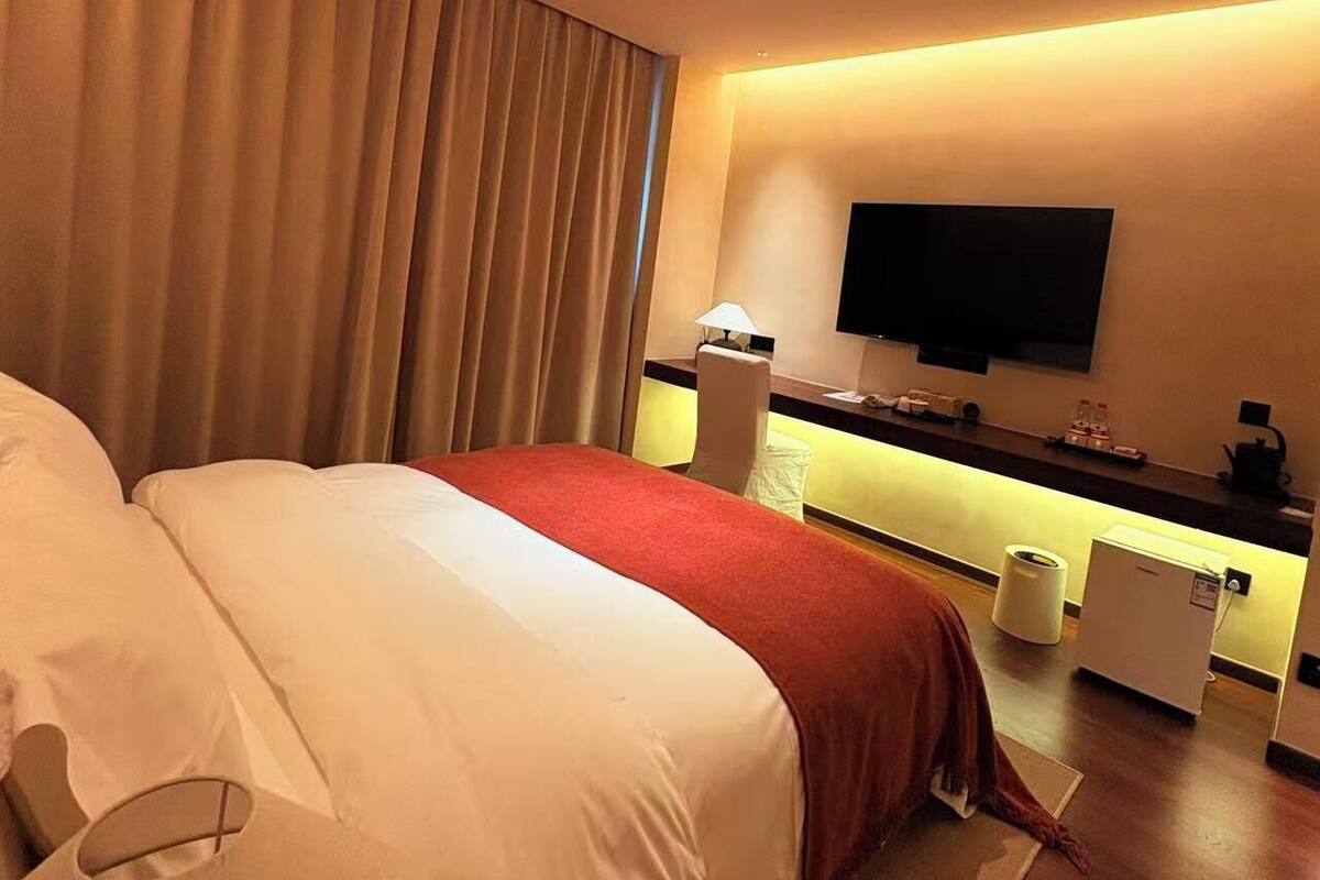 Una camera d'albergo con un letto grande, una scrivania con televisione a schermo piatto, un minibar e un bagno con il water e un lavandino.