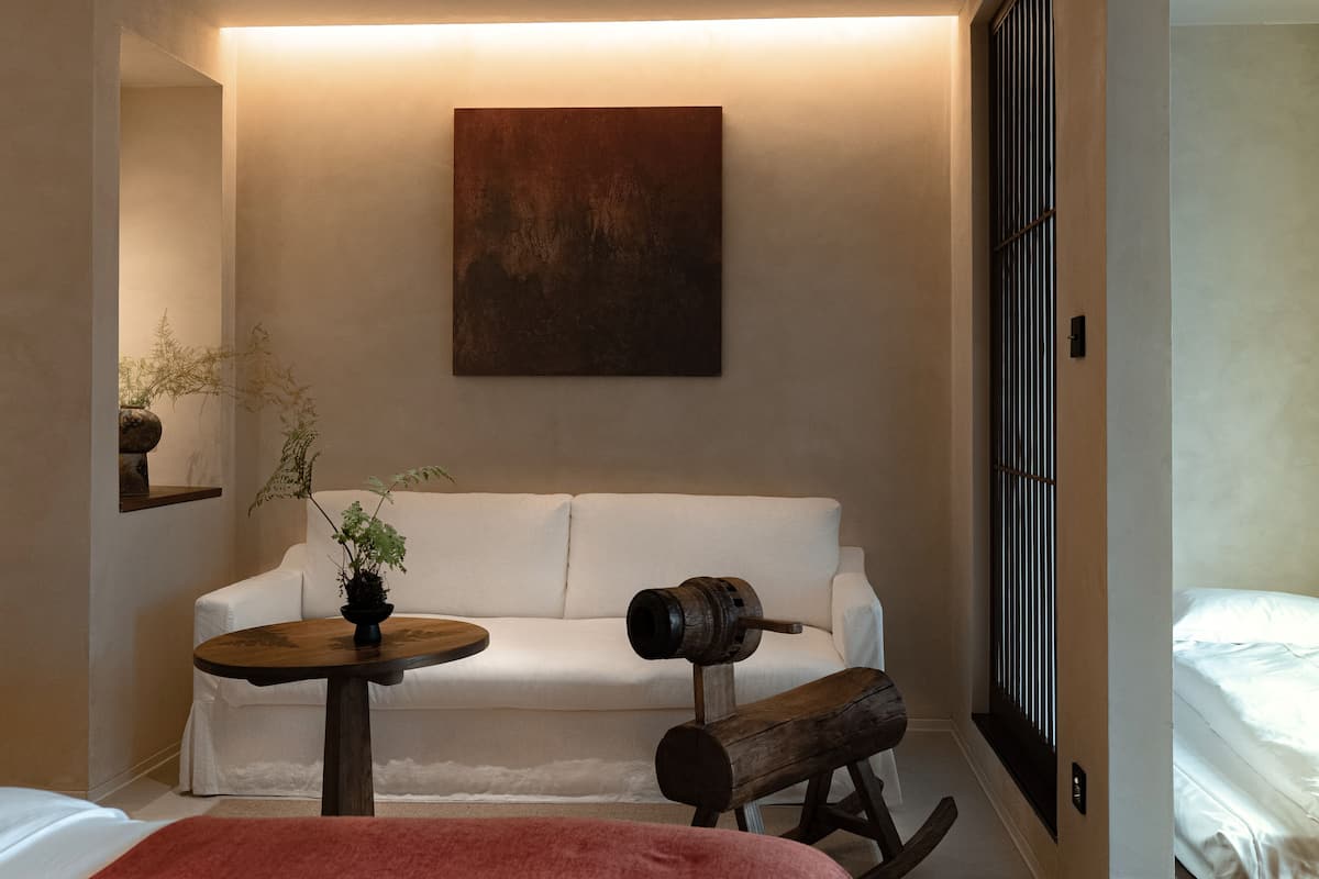 Una camera moderna con un divano bianco, una poltrona a dondolo in legno, un piccolo tavolino rotondo e un grande quadro astratto appeso al muro.