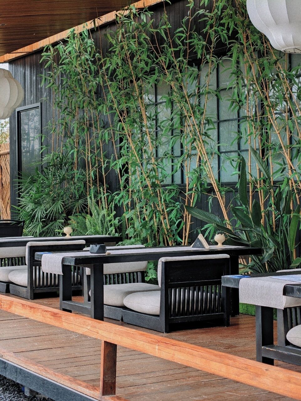 A row of black outdoor seating with cushions, a wooden deck, and a bamboo wall.