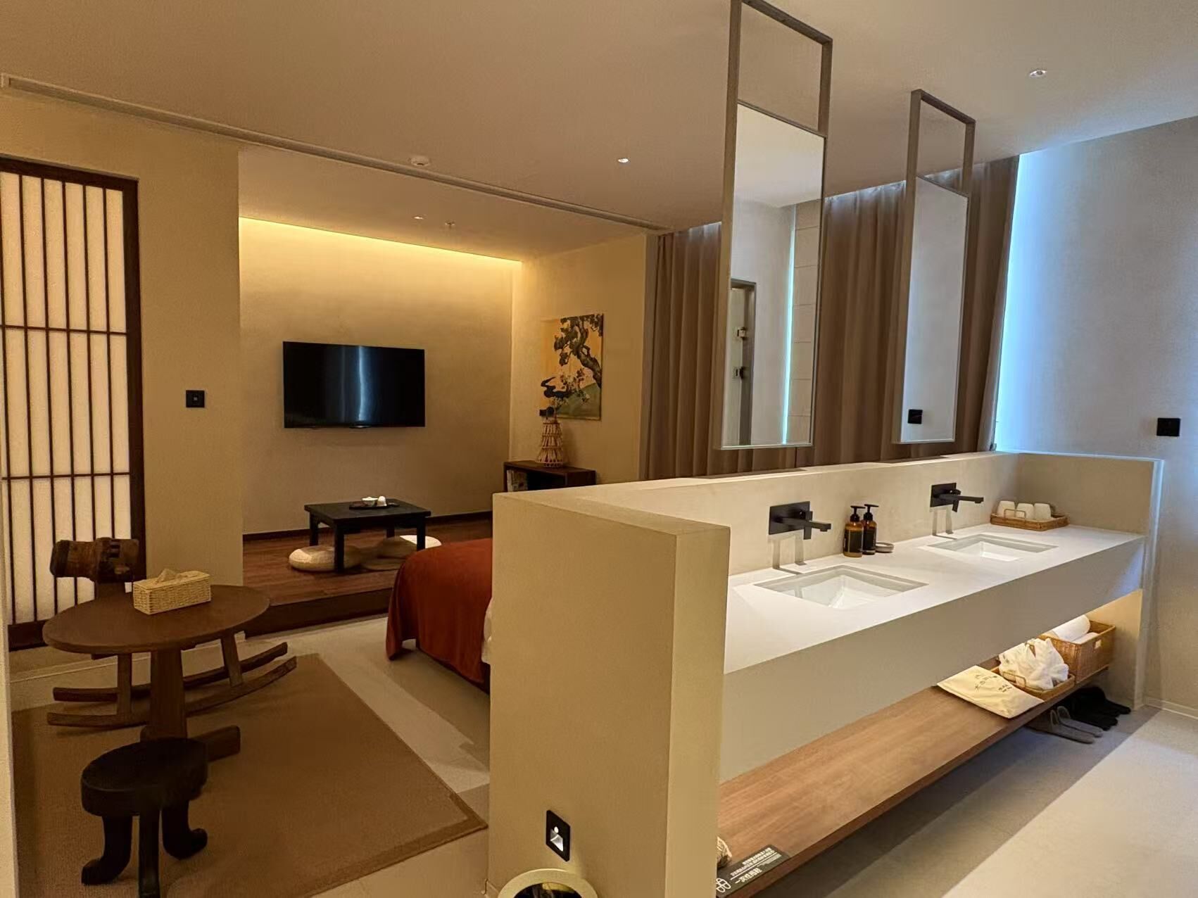 A modern hotel room with a large bathroom vanity, a flat-screen TV, a small dining area, and a traditional Japanese sliding door.